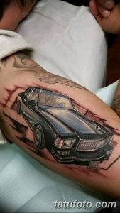 Фотография цветной татуировки на руке, изображающей классический автомобиль. Детализированный рисунок татуировки с реалистичными отражениями.