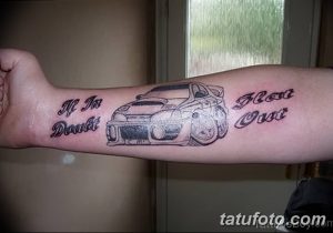 Фото тату на предплечье с изображением спортивного автомобиля и надписями 'He Ain't Doubt' и 'Flat Out' в готическом стиле.