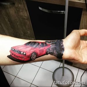Фотография татуировки BMW, оставляющей след из дыма, на мужской руке. Цветной рисунок, реалистичный стиль, динамичная композиция.