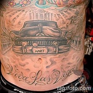 Фото тату на боку с изображением классического чёрного автомобиля и надписью 'Viva Las Vegas'. Рисунок выполнен в стиле чикано с использованием чёрных и серых оттенков.