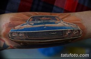 Фото тату: реалистичный рисунок синего Dodge Challenger на предплечье, выполненный в ярких цветах с эффектом пламени и брызг краски.