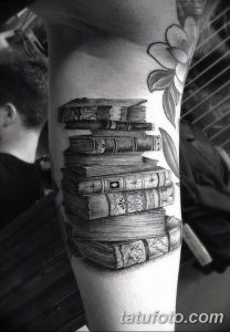 Фото тату: реалистичная стопка книг на предплечье, выполненная в черно-серых тонах с детальной проработкой обложек и страниц.
