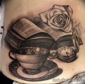 Фотография реалистичной татуировки на животе с изображением открытой книги, чашки чая, розы и карманных часов. Рисунок выполнен в черно-серых тонах с высокой детализацией.