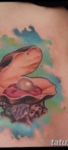 Фото тату раковины с жемчужиной на фоне морских волн. Реалистичный рисунок татуировки выполнен в мягких, пастельных тонах.