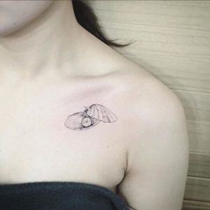 Фото тату раковины с жемчужиной на женской ключице. Нежный, минималистичный рисунок татуировки выполнен в черном цвете.