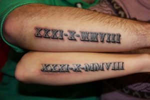 Фото двух запястий с одинаковыми татуировками, изображающими римские цифры 'XXXI-X-MMVIII'. Черный цвет, четкие линии. Символизирует важные даты.