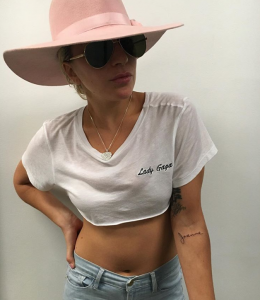 Фотография Леди Гаги в шляпе с татуировкой надписью "Joanne" на руке. Черно-белое изображение, демонстрирующее стильный образ певицы.