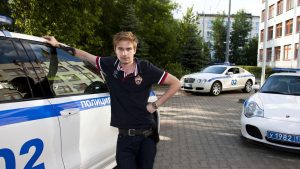 Фото известного человека с татуировкой на руке. Мужчина стоит рядом с полицейской машиной и автомобилем, демонстрируя свою татуировку.