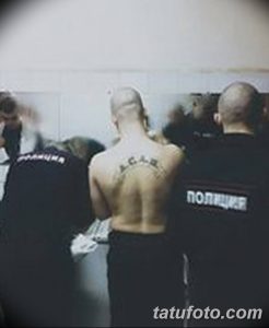 Фото тату надписи ACAB, выполненной готическим шрифтом на спине мужчины. Черный рисунок татуировки расположен дугой между лопатками.