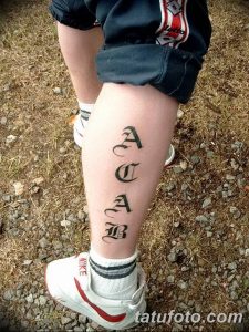 Фото тату надписи ACAB, выполненной готическим шрифтом на икре. Черный рисунок татуировки расположен вертикально вдоль ноги.