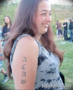 Фото тату надписи ACAB, выполненной готическим шрифтом на внутренней стороне предплечья девушки. Черный рисунок татуировки выглядит стильно и лаконично.