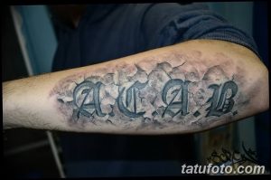 Фото татуировки 'ACAB', выполненной в стиле граффити на предплечье. Буквы стилизованы под трещины и обломки, создавая эффект разрушения.