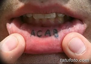 Фотография татуировки 'ACAB', выполненной черными чернилами на внутренней стороне губы. Необычное и провокационное расположение.