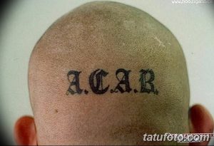 Фотография татуировки 'ACAB', выполненной черными чернилами на лысой голове. Минималистичный дизайн, четкие линии, небольшие размеры.