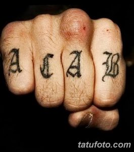 Фото татуировки на костяшках пальцев: надпись A.C.A.B. черным цветом. Минималистичный и провокационный рисунок татуировки.