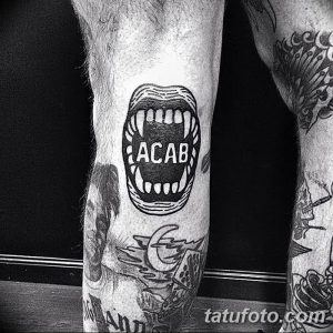 Фото тату надписи 'ACAB' внутри изображения зубов. Черно-белая татуировка, выражающая протест и смелость.