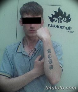 Фото тату: надпись 'ACAB' на руке, выполненная черными готическими буквами. Лицо человека частично скрыто.