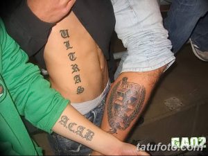 Фото тату: татуировки 'ACAB' на предплечье и 'ULTRAS' на боку, выполненные черными готическими буквами.