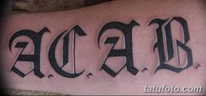 Фото тату с надписью 'ACAB' выполненной готическим шрифтом на предплечье. Татуировка выполнена в черных тонах.