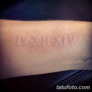 Фото тату на предплечье: римские цифры IV XII XIV, выполненные белыми чернилами. Необычный и минималистичный рисунок татуировки.