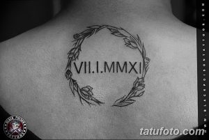 Фото тату на спине: римские цифры VII.I.MMXI заключены в венок из листьев и цветов. Черно-белая татуировка, минималистичный стиль.