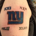 Фото тату на плече: логотип команды New York Giants с римскими цифрами, выполненный в ярких синих и красных цветах.