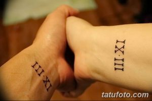 Фото тату на запястьях двух людей с изображением римских цифр, выполненное в минималистичном стиле черными чернилами. Символ любви и единства.