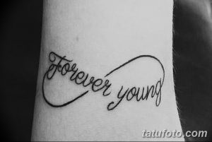 Фото тату с надписью 'Forever Young', заключенной в символ бесконечности на мужском предплечье. Четкие линии и минималистичный дизайн.