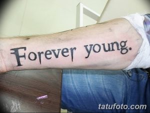 Фотография татуировки с надписью 'Forever Young', выполненной классическим шрифтом на предплечье. Стильный и мужественный рисунок татуировки.