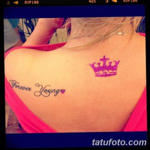 Фотография татуировки с надписью 'Forever Young' и изображением короны на спине. Яркий и выразительный рисунок татуировки для девушек.