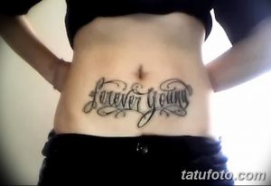 Фото тату надписи 'Forever Young' выполненной декоративным шрифтом на животе. Стильная и привлекательная татуировка.