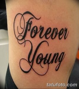 Фото тату надписи 'Forever Young' выполненной черными чернилами на предплечье. Изящный шрифт и четкие линии делают эту татуировку привлекательной.