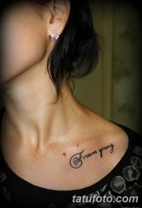 Фото татуировки надписи 'Forever Young' выполненной изящным шрифтом на женской груди.
