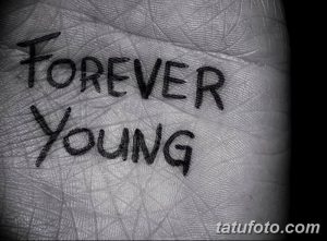 Фото тату с надписью 'Forever Young' на ладони. Минималистичная татуировка, выполненная черным цветом, подчеркивающая индивидуальность.