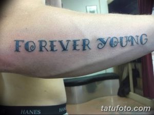 Фото тату на предплечье: надпись 'FOREVER YOUNG' выполненная необычным шрифтом с использованием заглавных и строчных букв.