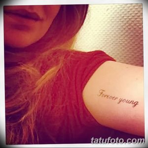 Фото тату на плече: надпись 'Forever Young' выполненная золотистым цветом, на фоне кожи.