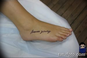 Фото тату с надписью 'Forever Young' на стопе, выполненной тонким черным шрифтом. Изящный дизайн на светлой коже.