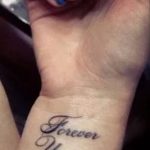 Фото тату с надписью 'Forever Young' на запястье, выполненной изящным черным шрифтом. Минималистичный дизайн на светлой коже.