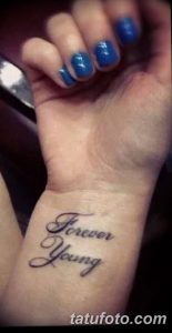 Фото тату с надписью 'Forever Young' на запястье, выполненной изящным черным шрифтом. Минималистичный дизайн на светлой коже.