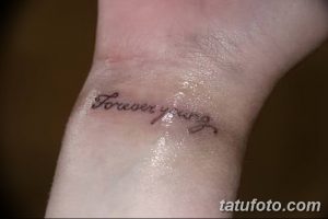 Фото тату с надписью 'Forever Young' на запястье, выполненной тонким черным шрифтом. Минималистичный рисунок на светлой коже.