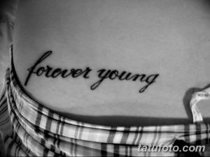 Фото тату с надписью 'Forever Young' на боку, выполненной тонким черным контуром. Изящный шрифт на светлой коже.