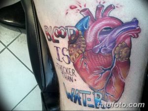 Фото тату анатомического сердца на бедре, с надписью "Blood is thicker than water". Детализированный рисунок татуировки в реалистичном стиле.