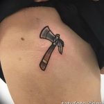 Фото тату на плече: минималистичный рисунок томагавка, выполненный в черном цвете с использованием простых линий.