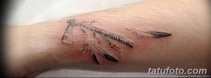 Небольшая татуировка томагавка с перьями, выполненная в минималистичном стиле на запястье. Тонкие линии, реалистичная детализация.