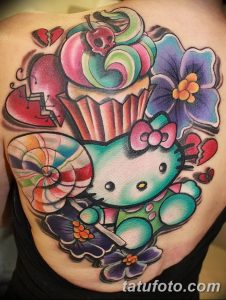 Фото тату на плече: красочная Hello Kitty в окружении цветов и разбитого сердца. Татуировка выполнена в стиле олд скул с яркими контурами и насыщенными цветами.