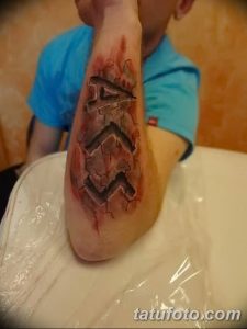 Фото тату на предплечье с изображением головы дракона, словно вырывающейся из кожи. Реалистичная проработка чешуи, когтей и текстуры кожи.
