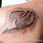Фото тату символа гильдии Fairy Tail на плече, выполненное в черно-белой гамме. Детализированный рисунок татуировки с эффектом разбитой кожи.