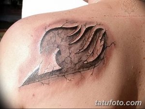 Фото тату символа гильдии Fairy Tail на плече, выполненное в черно-белой гамме. Детализированный рисунок татуировки с эффектом разбитой кожи.