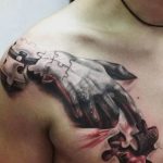 Фото татуировки руки, словно вырывающейся из пазла, на груди. Реалистичный рисунок с элементами сюрреализма и детализированными тенями.