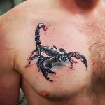 Фото тату скорпиона на груди мужчины. Детализированный рисунок черного скорпиона с красными акцентами, выполненный в реалистичном стиле.